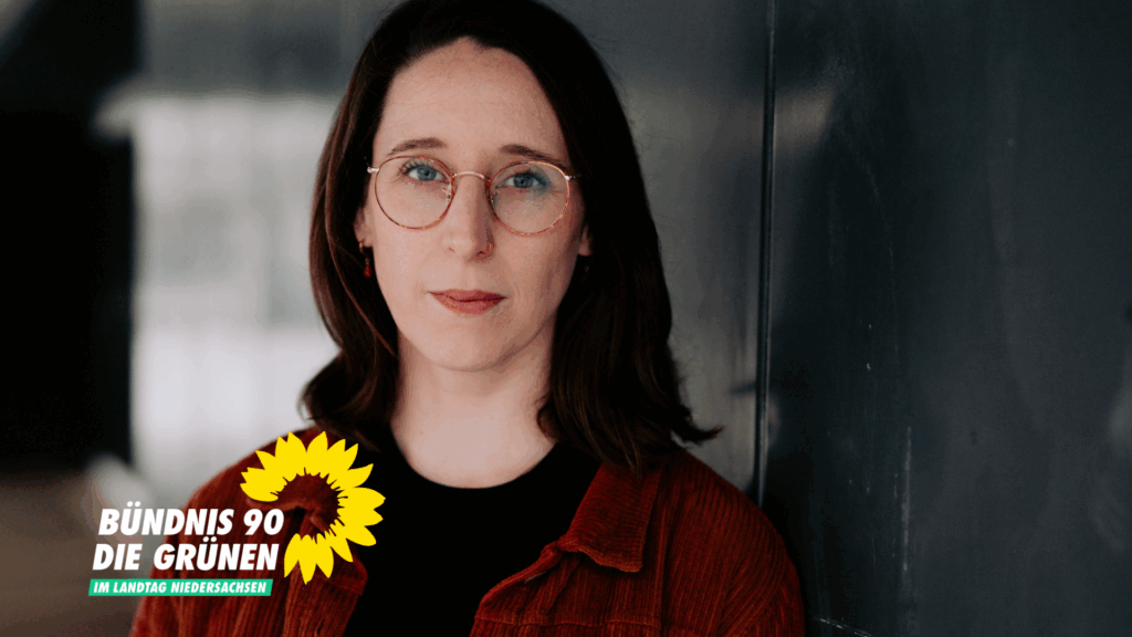 Swantje Schendel lehnt an einer dunkelgrauen Wand und schaut dich mit einem ernsten Lächeln an.