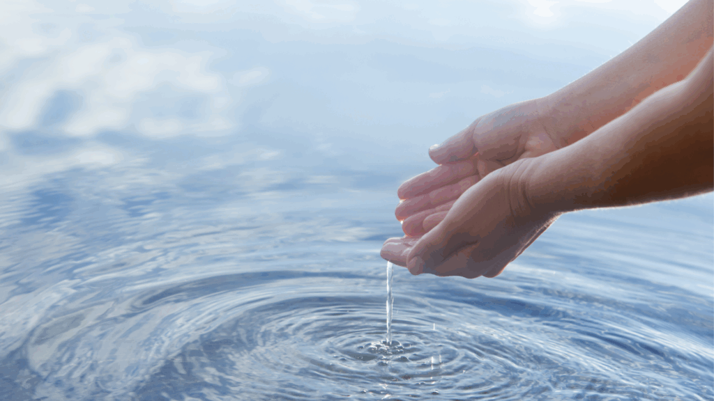 Zwei Hände lassen Wasser in einen See tropfen.
