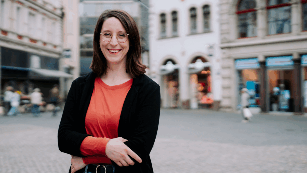 Swantje Schendel steht mit verschränkten Armen auf dem Kohlmarkt in Braunschweig und blickt dich mit einem Lächeln optimistisch an.