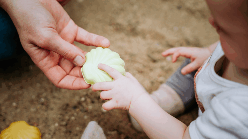 Eine Erwachsenen- und eine Kinderhand halten gemeinsam ein grünes Sandförmchen.