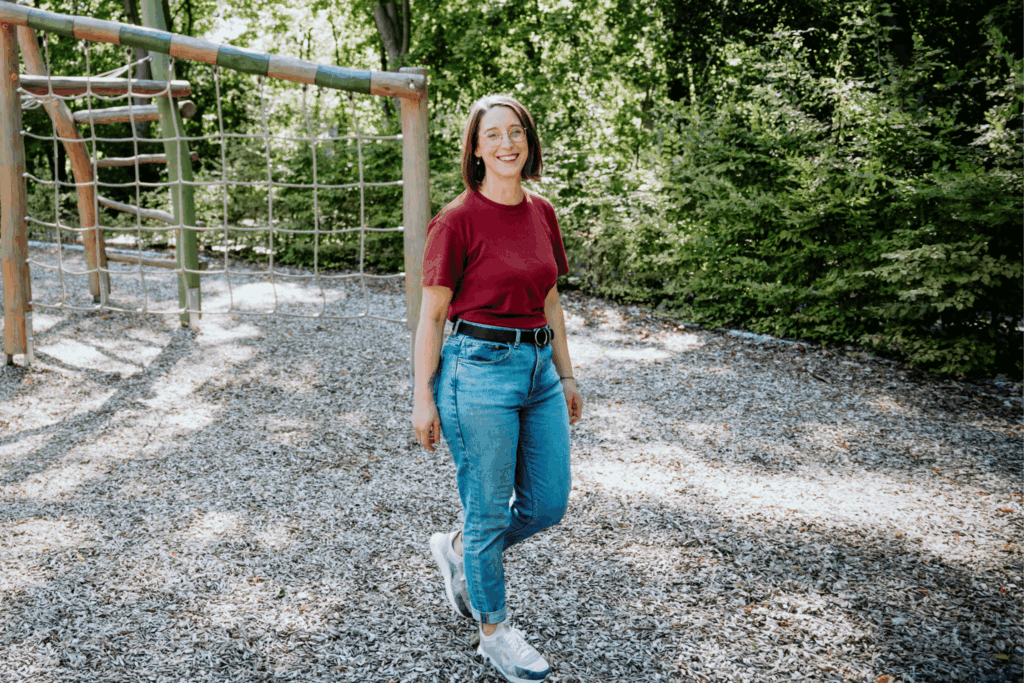 Swantje Schendel spaziert im Sommer über einen Spielplatz. Die Sonne scheint, sie schaut den Betracher fröhlich an.